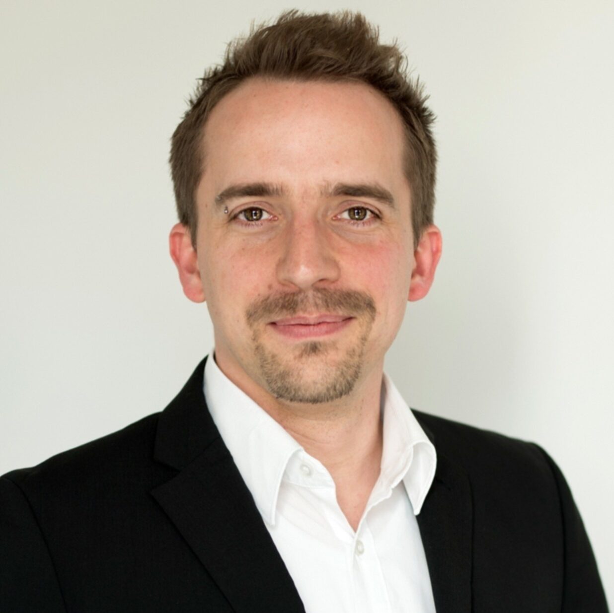 Das Bild zeigt einen Mann mit einem drei Tage Bart und mittelblondem Haar. Er trägt ein weißes Hemd, einen schwarzen Anzug.  Es handelt sich um Prof. Dr. Malte Weiß der im Transferhub arbeitet.